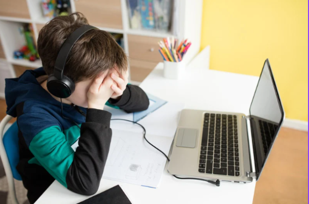Young boy looking frustrated during homeschooling with laptop and headphones on.