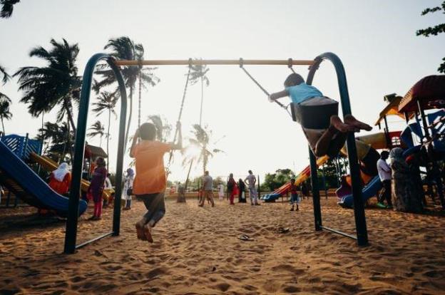 Children playing on swings at a community playground with families in the background during sunset.