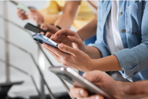 A person holding a smartphone in a dimly lit setting, reflecting late-night screen use and digital distraction.